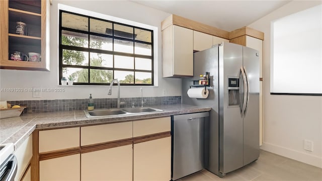 kitchen with baseboards, cream cabinets, appliances with stainless steel finishes, and a sink