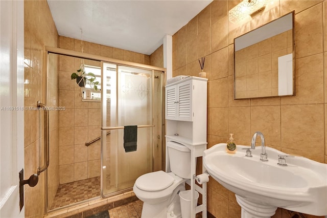 bathroom featuring tile walls, toilet, a stall shower, and a sink