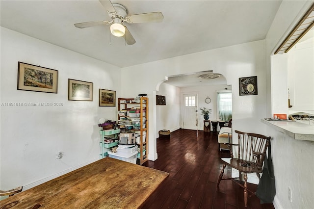 interior space featuring arched walkways, baseboards, dark wood-type flooring, and a ceiling fan