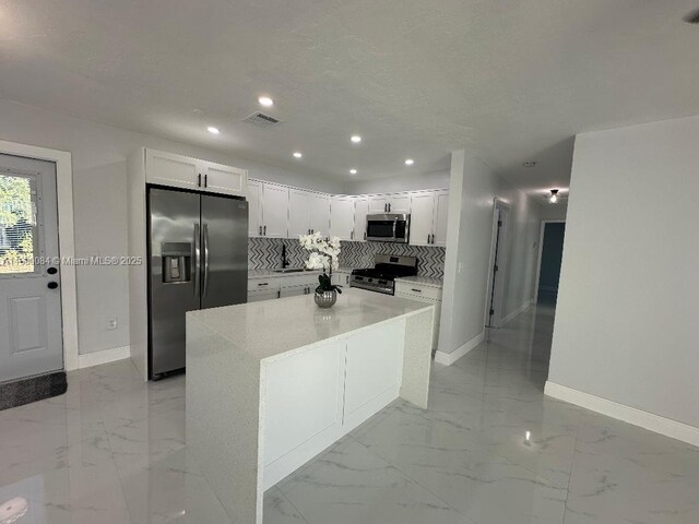 kitchen featuring appliances with stainless steel finishes, a center island, tasteful backsplash, and white cabinetry