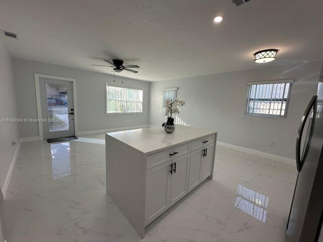 kitchen featuring white cabinets, stainless steel fridge, a kitchen island, and ceiling fan