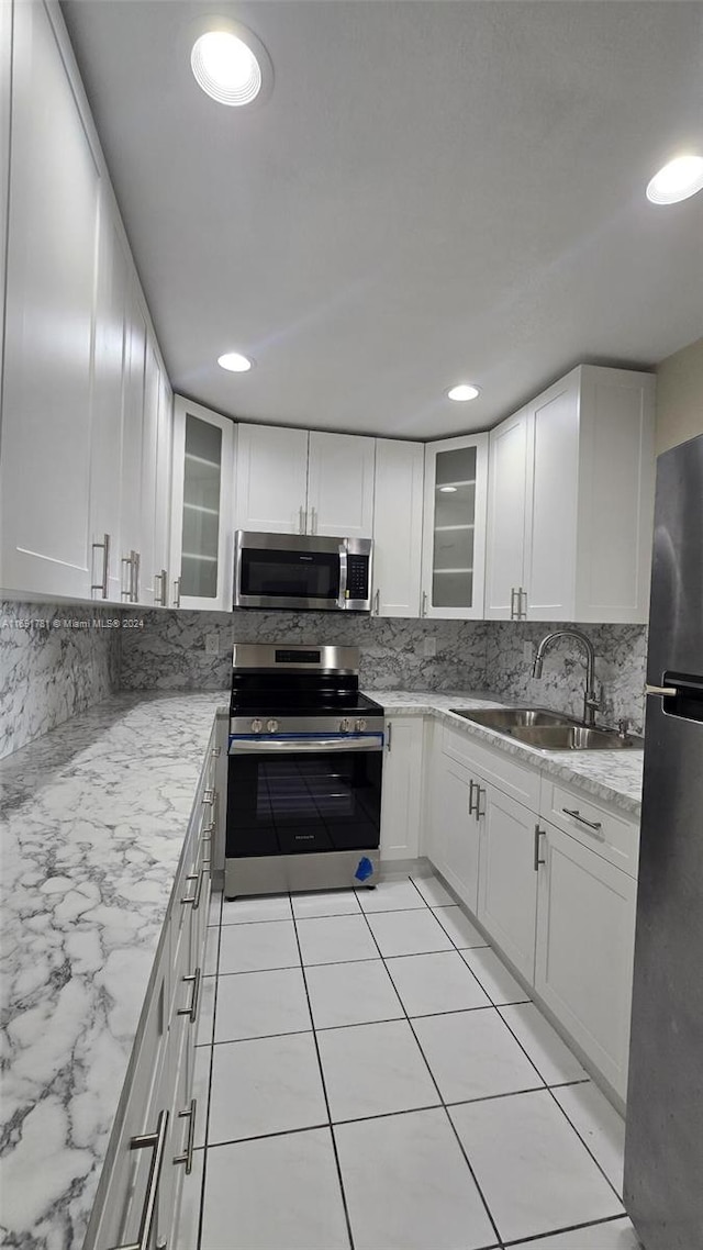 kitchen featuring light stone counters, backsplash, appliances with stainless steel finishes, sink, and white cabinets