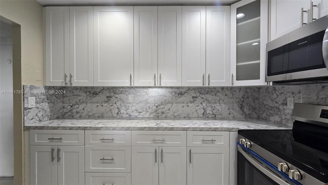 kitchen featuring white cabinetry, stainless steel appliances, light stone counters, and backsplash