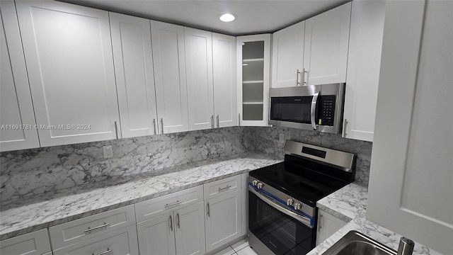 kitchen with stainless steel appliances, light stone countertops, white cabinets, and tasteful backsplash