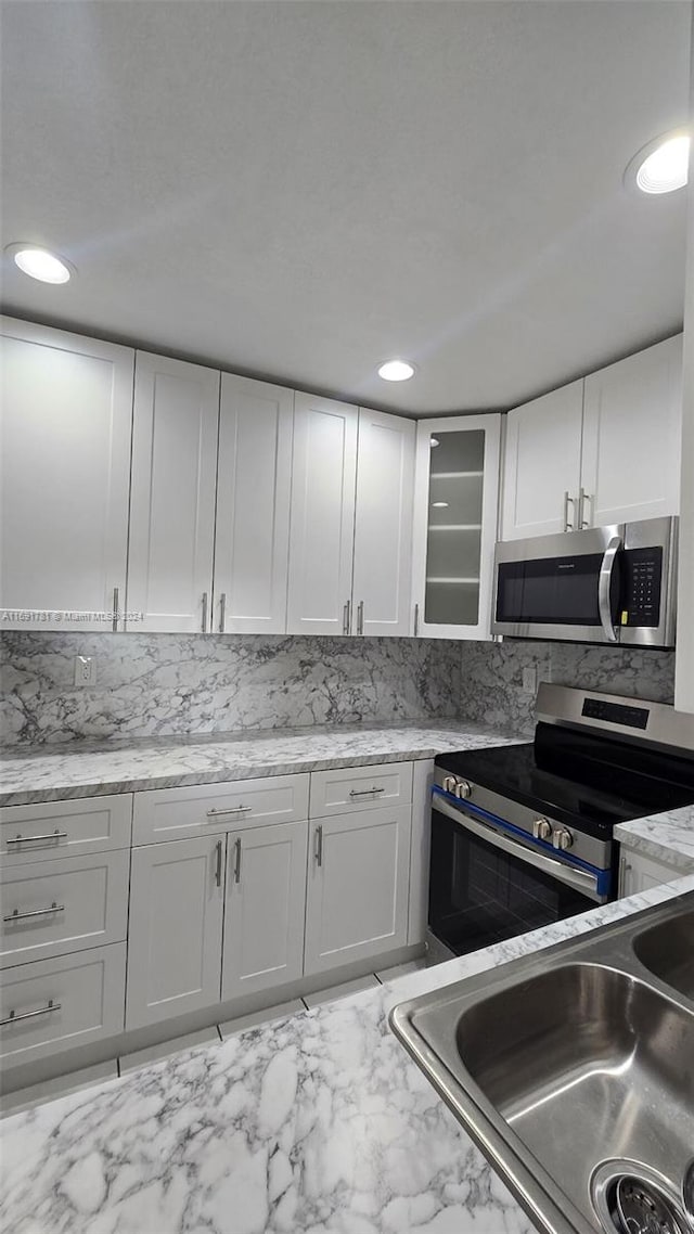 kitchen with white cabinetry, stainless steel appliances, sink, and light stone counters