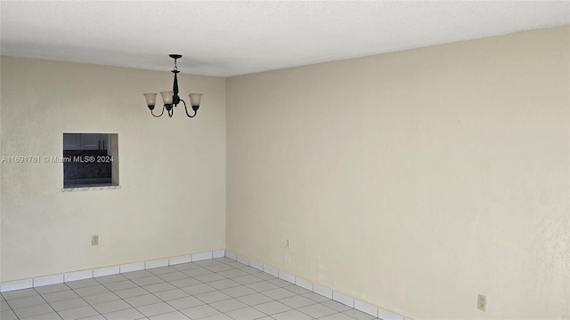 tiled spare room with a textured ceiling and an inviting chandelier