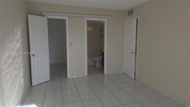 unfurnished bedroom with ensuite bathroom, light tile patterned floors, and a closet