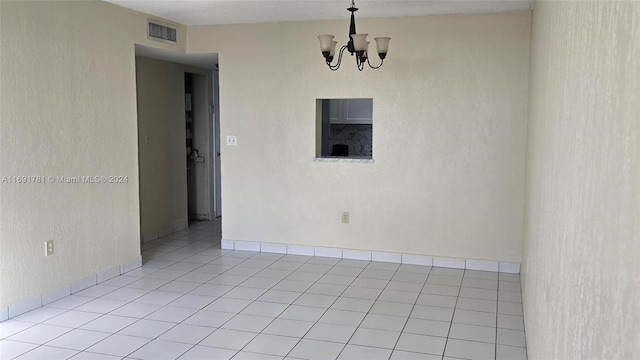 empty room with light tile patterned floors and an inviting chandelier