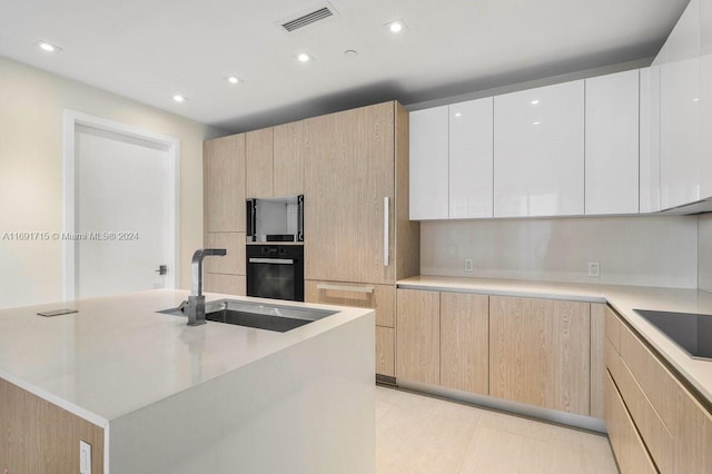 kitchen featuring light brown cabinetry, black appliances, sink, white cabinetry, and an island with sink