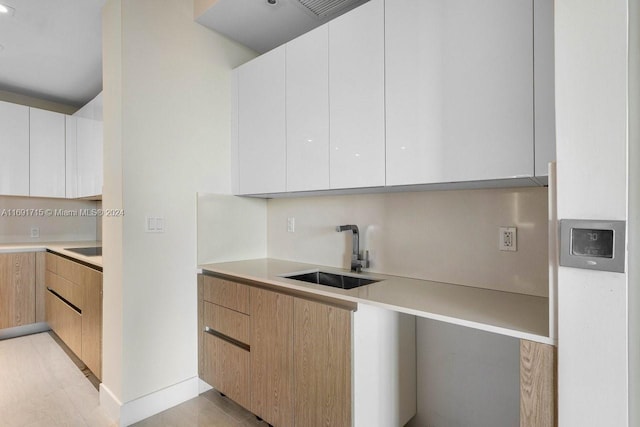 kitchen featuring white cabinets, light brown cabinets, and sink