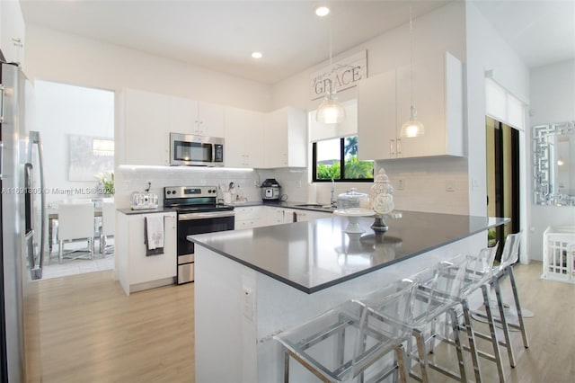 kitchen with hanging light fixtures, light wood-type flooring, a kitchen bar, white cabinetry, and stainless steel appliances