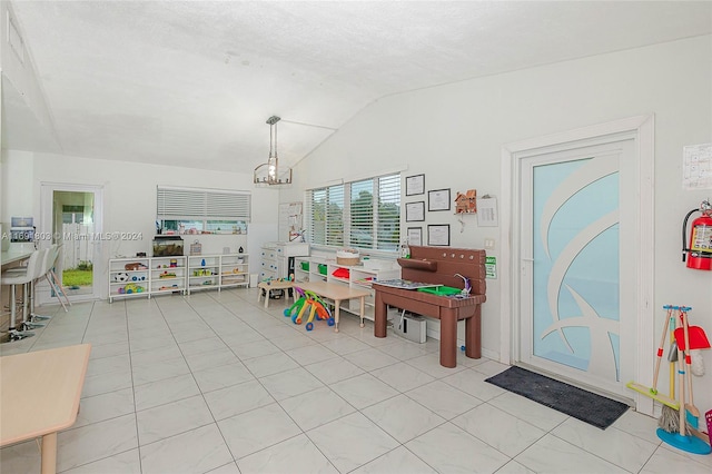 game room with a textured ceiling, a chandelier, vaulted ceiling, and light tile patterned flooring