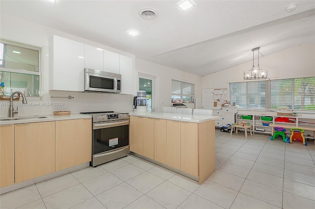 kitchen featuring vaulted ceiling, kitchen peninsula, sink, appliances with stainless steel finishes, and decorative light fixtures