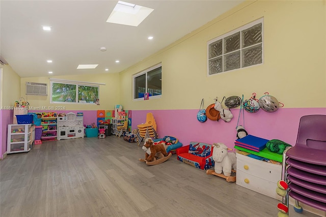 recreation room featuring hardwood / wood-style floors, an AC wall unit, and vaulted ceiling with skylight