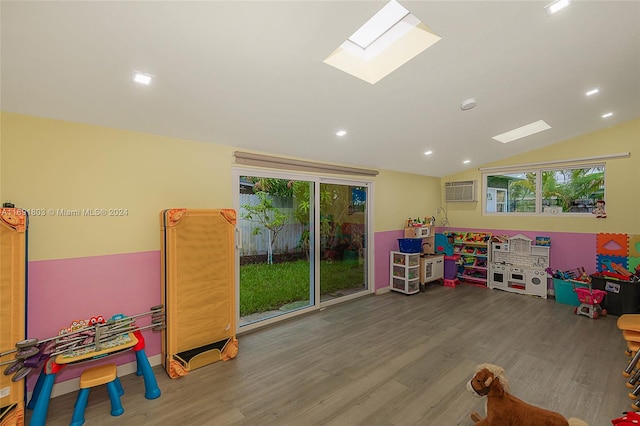 playroom featuring lofted ceiling with skylight, hardwood / wood-style flooring, a wall mounted AC, and plenty of natural light