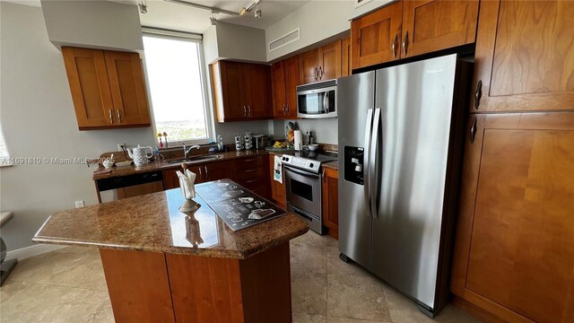 kitchen with sink, rail lighting, stainless steel appliances, a kitchen island, and dark stone counters