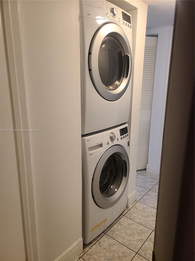 laundry room featuring light tile patterned floors, stacked washing maching and dryer, and a textured ceiling