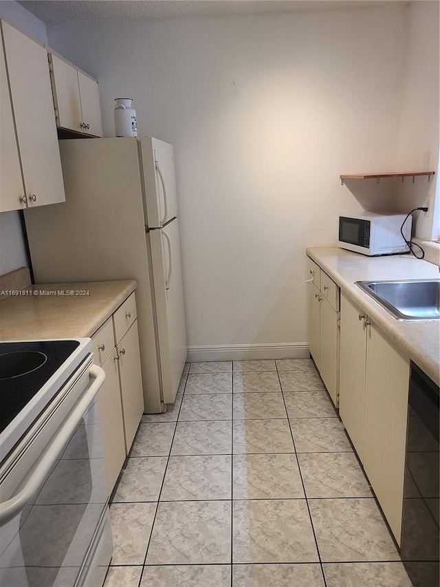 kitchen with white cabinetry, sink, light tile patterned floors, and white appliances