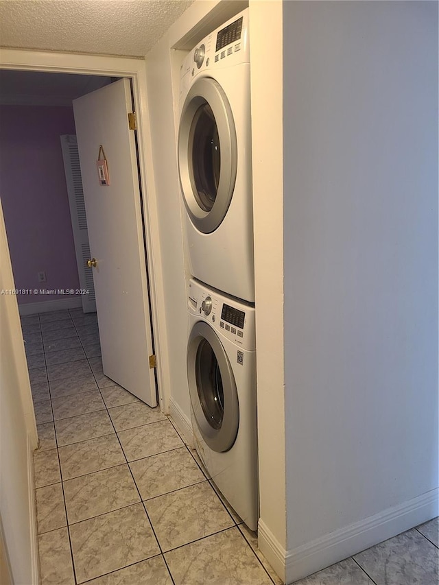 laundry area with a textured ceiling, stacked washer / dryer, and light tile patterned flooring