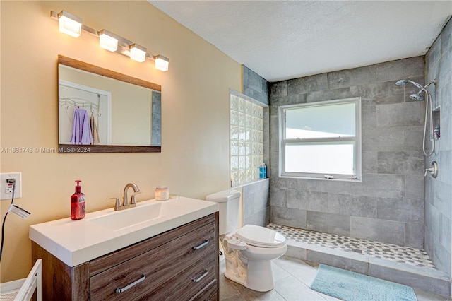 bathroom with toilet, tiled shower, vanity, and tile patterned floors