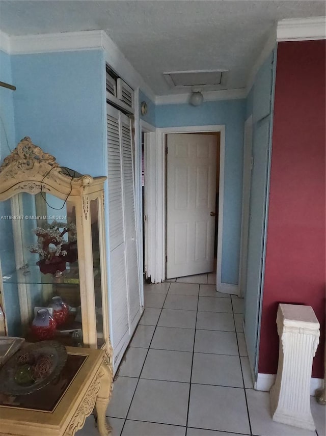 corridor with a textured ceiling, light tile patterned floors, and ornamental molding