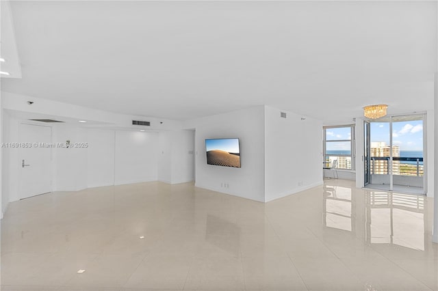 tiled empty room featuring a chandelier and a wall of windows