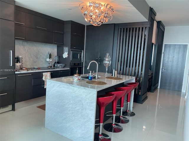 kitchen featuring a center island with sink, sink, black oven, a breakfast bar area, and stainless steel microwave