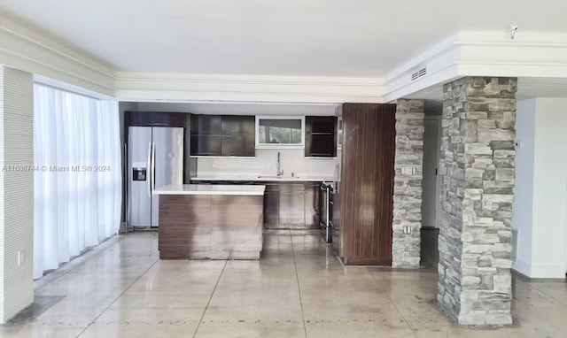 kitchen with dark brown cabinets, stainless steel refrigerator with ice dispenser, sink, decorative columns, and a center island