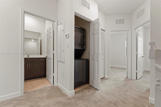 hallway with stacked washing maching and dryer and light colored carpet