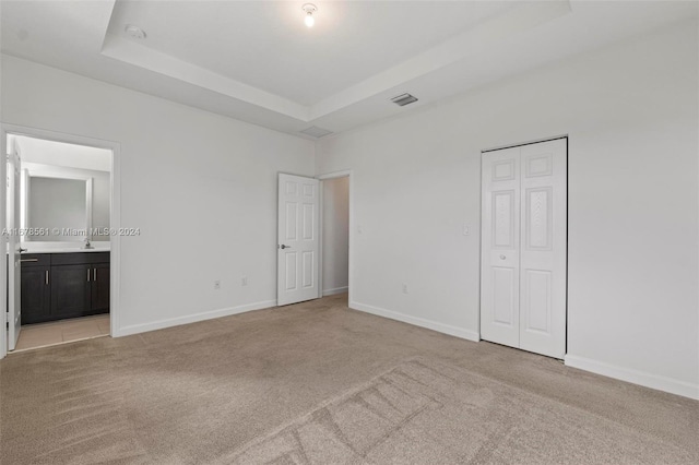 unfurnished bedroom with ensuite bathroom, light colored carpet, a raised ceiling, and a closet