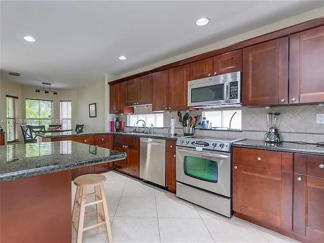 kitchen featuring a kitchen bar, light tile patterned flooring, backsplash, appliances with stainless steel finishes, and dark stone countertops