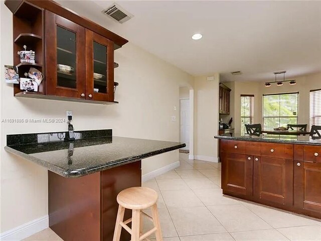 kitchen with kitchen peninsula, a breakfast bar area, dark stone countertops, and light tile patterned floors