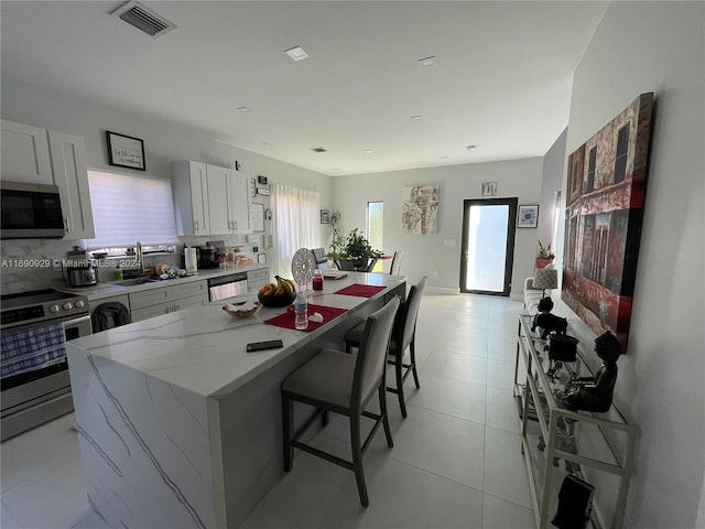 kitchen with a kitchen bar, a center island, white cabinets, backsplash, and appliances with stainless steel finishes