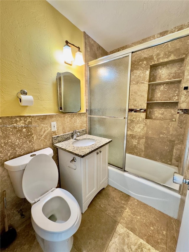 full bathroom featuring toilet, combined bath / shower with glass door, tile walls, and vanity