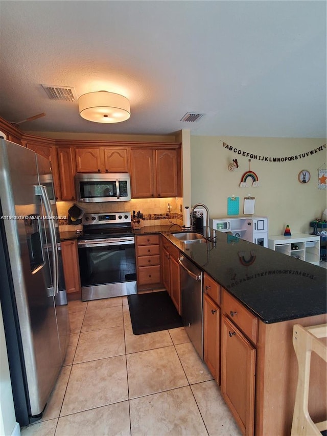 kitchen with light tile patterned flooring, appliances with stainless steel finishes, sink, dark stone countertops, and kitchen peninsula