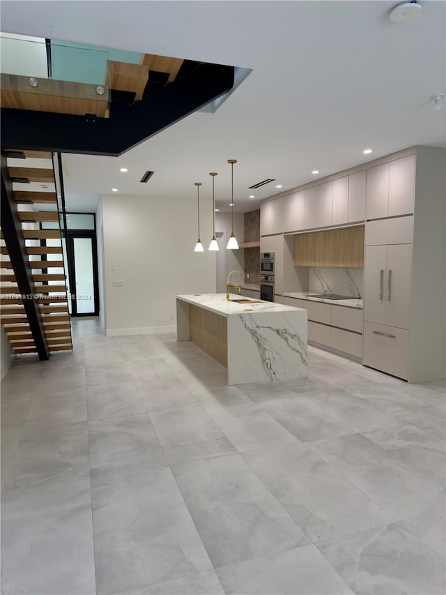 kitchen featuring hanging light fixtures, sink, stainless steel double oven, an island with sink, and light stone countertops