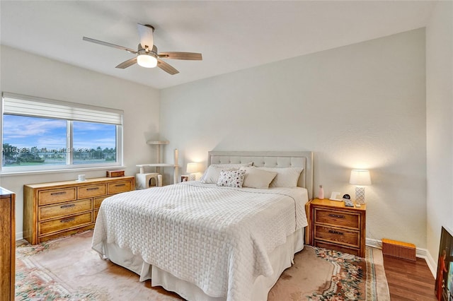 bedroom featuring ceiling fan, light hardwood / wood-style flooring, and a water view