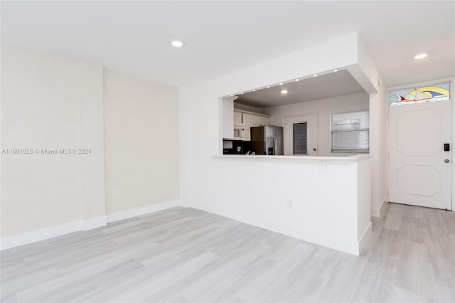 kitchen with light hardwood / wood-style flooring, kitchen peninsula, stainless steel refrigerator, and white cabinets