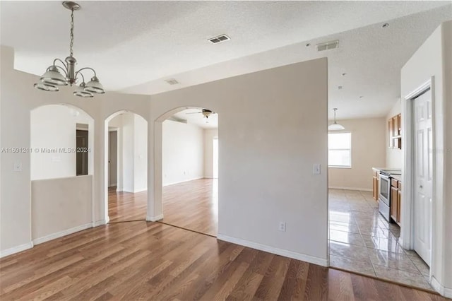 empty room with a textured ceiling, ceiling fan with notable chandelier, and hardwood / wood-style flooring