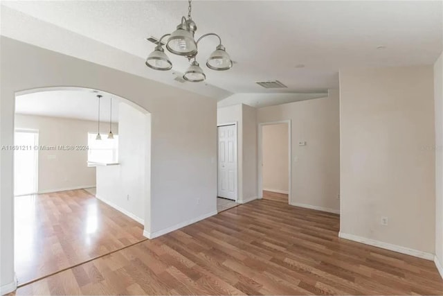 unfurnished room with wood-type flooring, lofted ceiling, and a notable chandelier