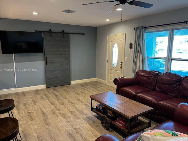 living room featuring a barn door, light hardwood / wood-style flooring, and ceiling fan