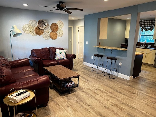 living room with ceiling fan, wet bar, and light wood-type flooring