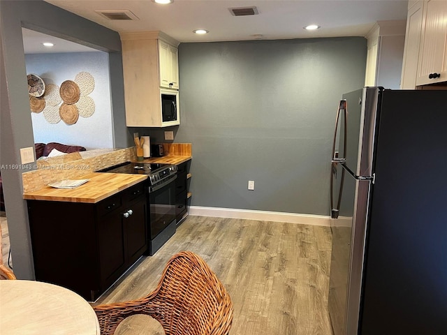 kitchen with white cabinets, light hardwood / wood-style floors, wood counters, and black appliances