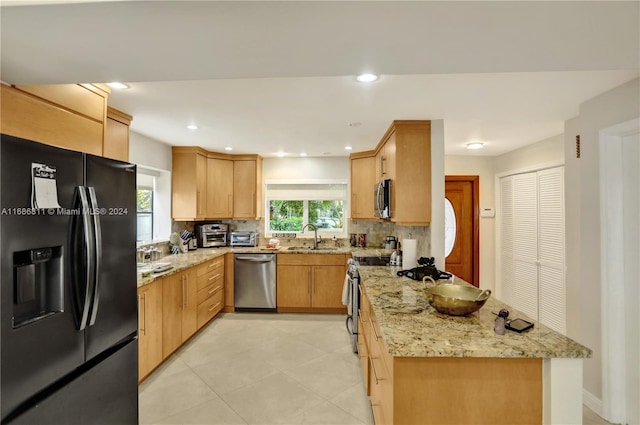 kitchen featuring light stone counters, kitchen peninsula, sink, backsplash, and appliances with stainless steel finishes