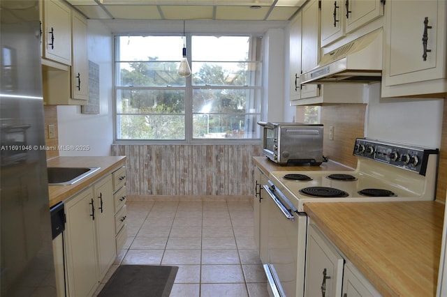 kitchen with sink, wooden walls, light tile patterned floors, white range with electric stovetop, and stainless steel refrigerator