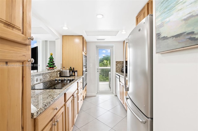 kitchen with light stone countertops, black electric cooktop, stainless steel refrigerator, and light tile patterned flooring