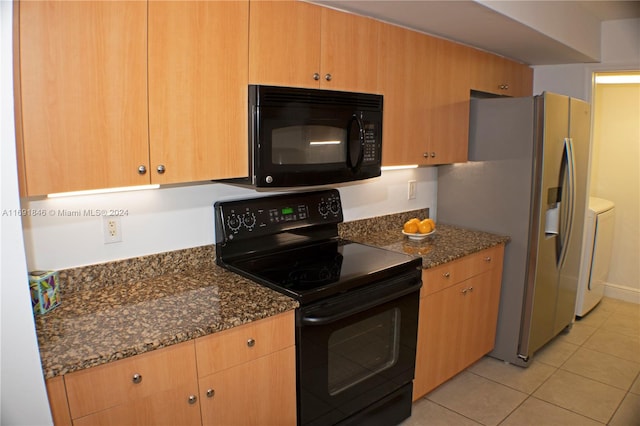 kitchen with washing machine and dryer, dark stone countertops, light tile patterned floors, and black appliances