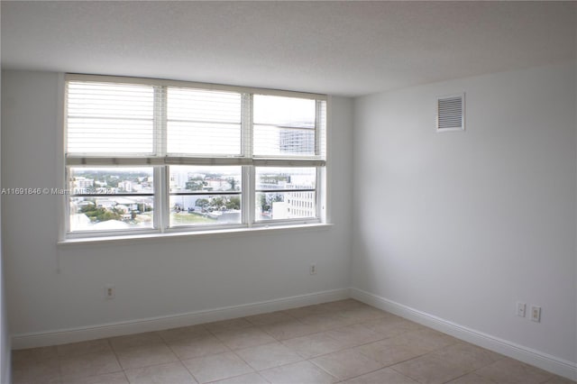 empty room with a textured ceiling, a wealth of natural light, and light tile patterned flooring