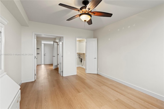 unfurnished bedroom featuring a closet, light wood-type flooring, a spacious closet, and ceiling fan