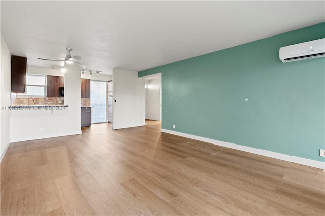 unfurnished living room featuring a wall unit AC, sink, and light hardwood / wood-style flooring